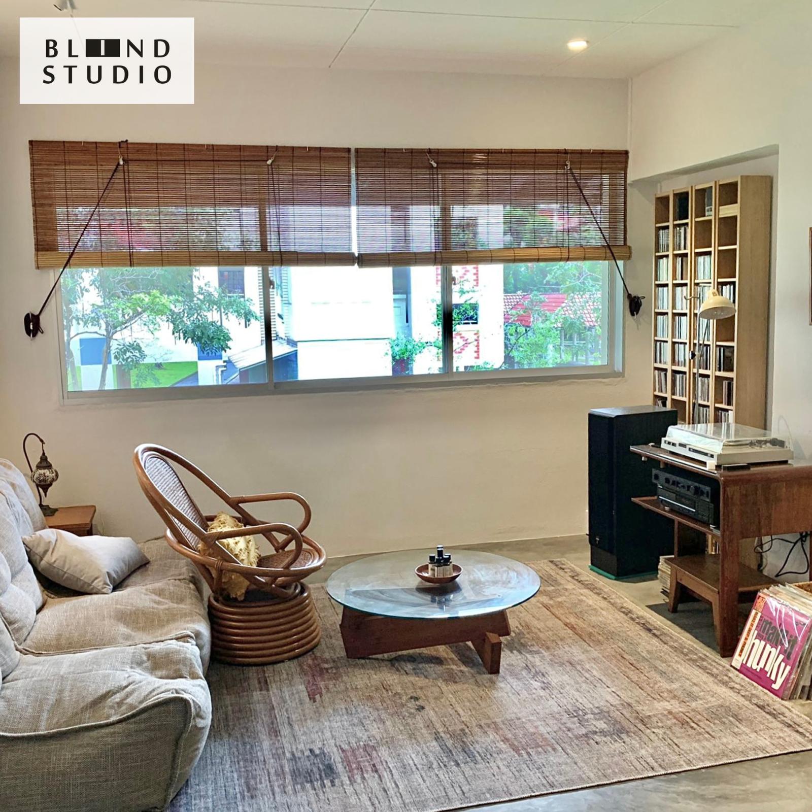 Natural Color Bamboo Blinds in a living room with a ratten chair, grey sofa and a wooden bookshelf